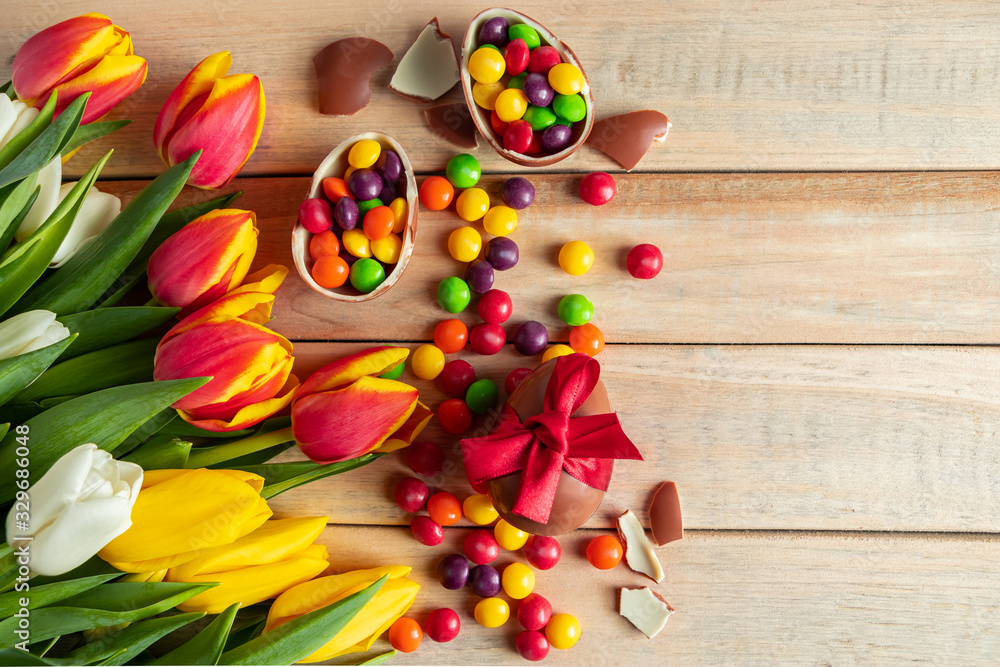 Multi-colored tulips and chocolate Easter eggs on a wooden background. Festive design, place for text.