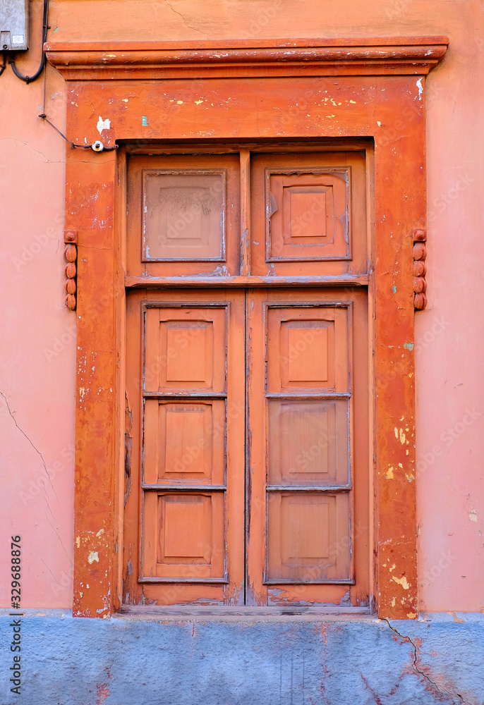 A simple closed wooden old window in a red and pink painted wall.
