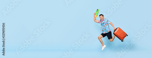 Jumping handsome Asian tourist man traveling with water gun and baggage during Songkran festival on banner blue background with copy space