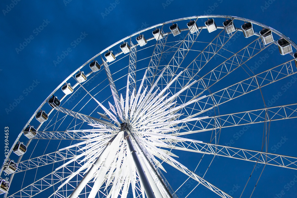 View from base of big and beautiful Ferris wheel slowly rotate to let tourists / travelers enjoy high view of cityscape sky during relaxing twilight sky in fun fair in city. View from base of big and beautiful Ferris wheel slowly rotate to let tourists / travelers enjoy high view of cityscape sky during relaxing twilight sky in fun fair in city.