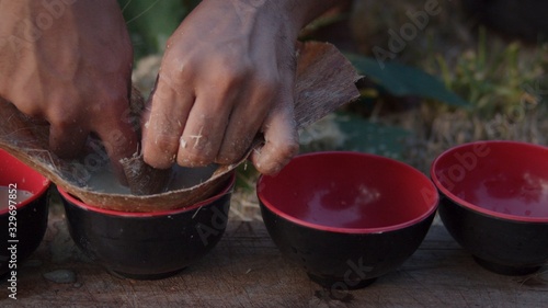 local young black man preparing kava juice drink at a tropical island of Vanuatu in the south pacific ocean during the afternoon by squeezing it to small cups