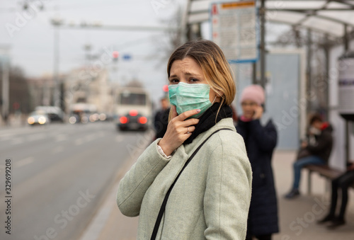 Sad woman wearing medical mask ill by the virus in the city street at the bus station. © hbrh