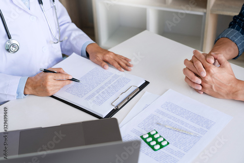 doctor working with patient taking notes with clipboard and discussing something in his medical office, health care and people concept.
