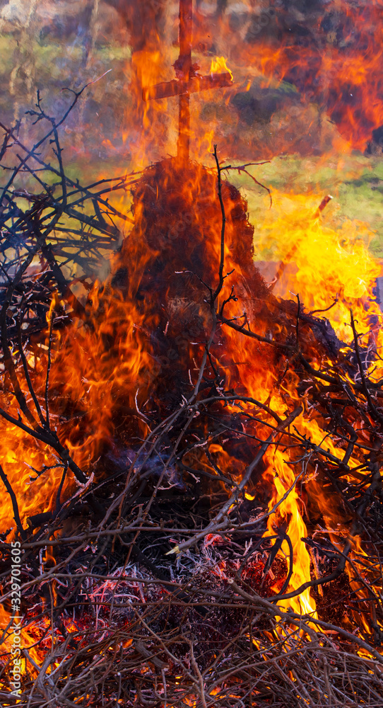Flaming fire. Big bonfire in Shrovetide. Burning tree branches. People look at the fire. Pagan rite dedicated to the arrival of spring. Flaming fire. Big bonfire in Shrovetide. Burning tree branches. People look at the fire. Pagan rite dedicated to the arrival of spring.