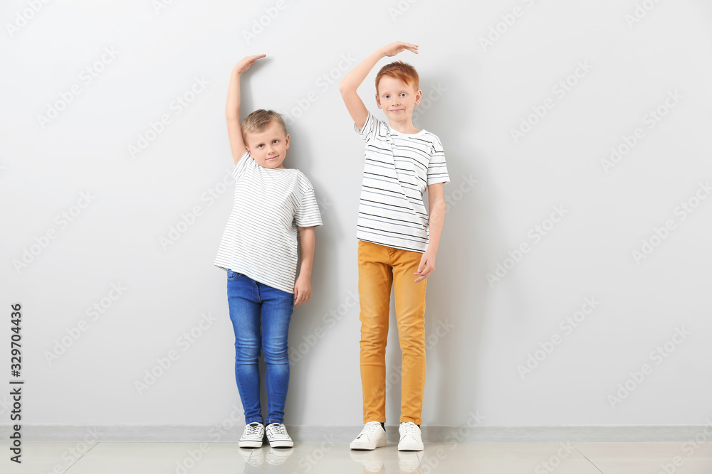 Cute little boys measuring height near light wall Cute little boys measuring height near light wall