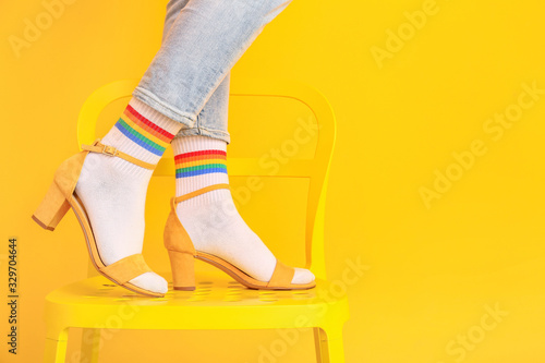 Legs of young woman in socks and sandals standing on chair against color background