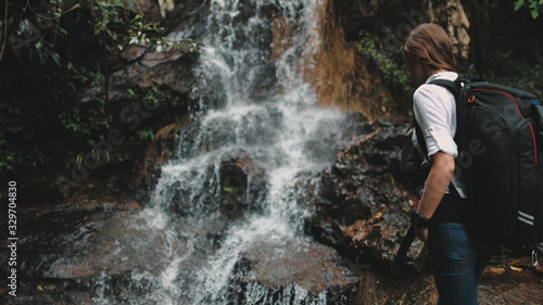Woman Tourist Reach out to Splashing Waterfall. Active Caucasian Young Girl with Backpack Hike at Beautiful Thailand Canyon. Water Flowing on Rocks. Tropical Vacation.