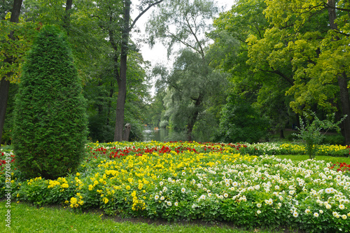 Fototapeta Naklejka Na Ścianę i Meble -  St. Petersburg in summer. Beautiful city park with flower beds and green trees near the pond on Elagin Island. In the distance, people relax in boats on a pond. Park landscape