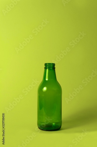 Small empty green glass bottle without cover and label on bright green background. Can be used as mock up for juice or beer.