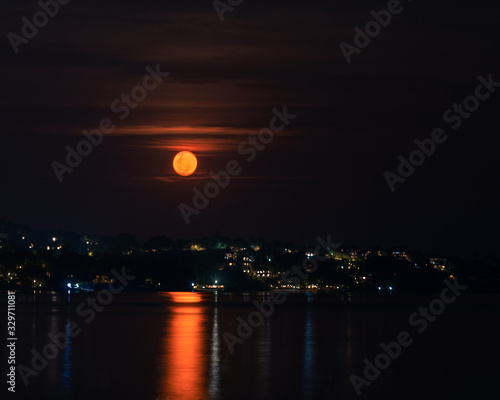 Red full moon in the night sky over sea and houses on the beach 