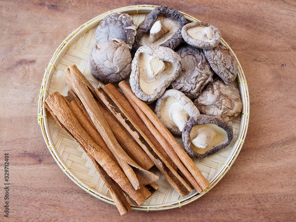 Top view of dried cinnamon sticks and dry shiitake mushrooms in bamboo weave tray on wooden table. Top view of dried cinnamon sticks and dry shiitake mushrooms in bamboo weave tray on wooden table.