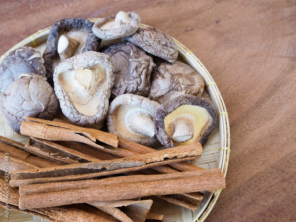 Top view of dried cinnamon sticks and dry shiitake mushrooms in bamboo weave tray on wooden table. Top view of dried cinnamon sticks and dry shiitake mushrooms in bamboo weave tray on wooden table.