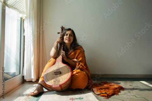 Woman sitting by the window and practicing music on her tambura.   photo