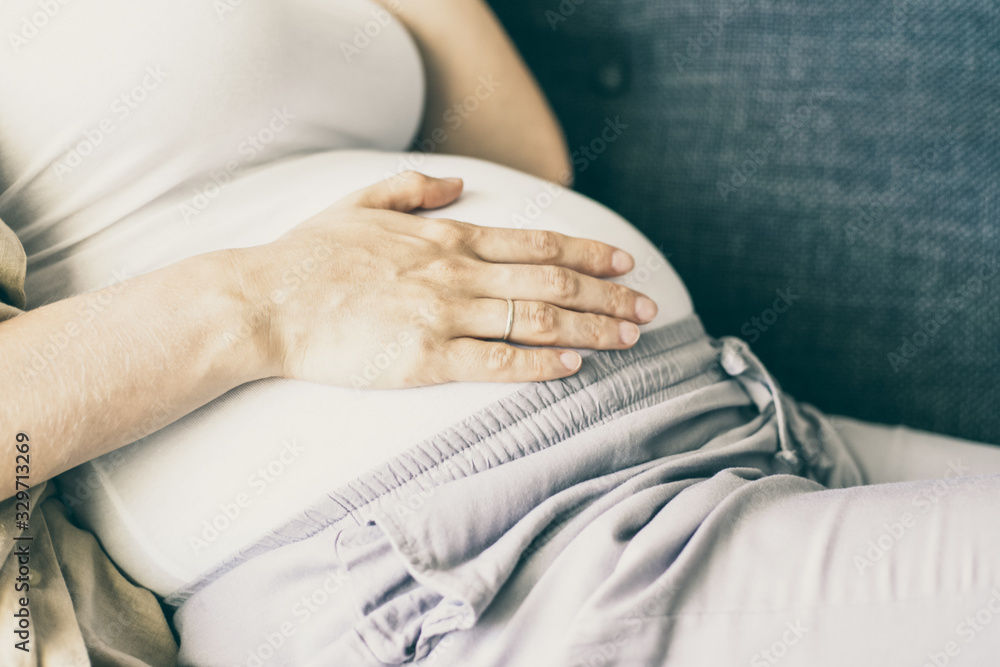 Fototapeta premium Expectant mother relaxing at home. Baby bump of pregnant woman wearing comfortable clothes, lying on couch. Pregnancy concept