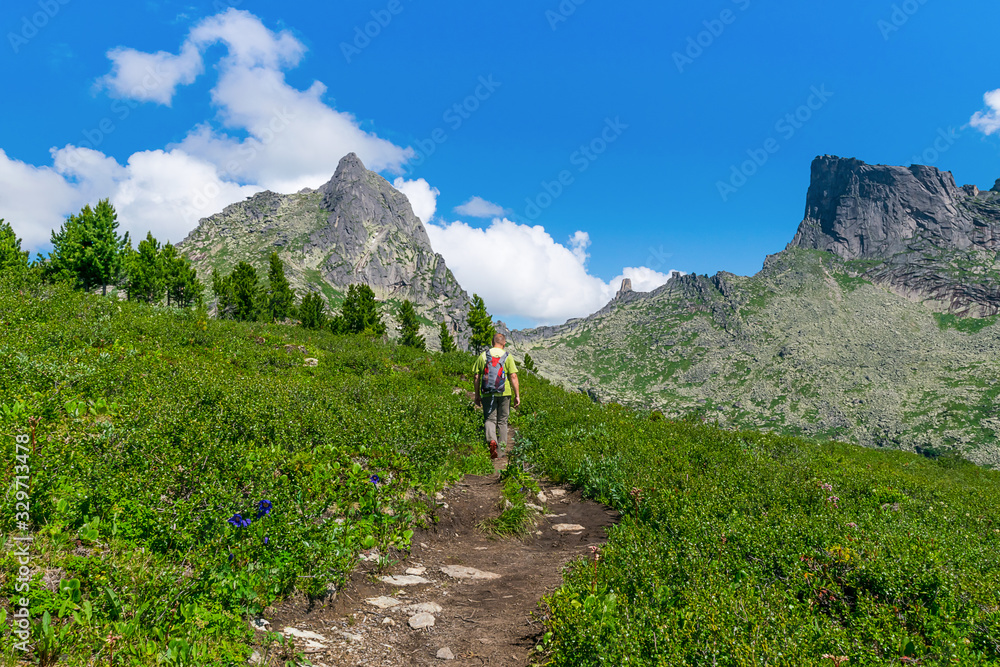 A man with backpack goes along a rocky path to the rocks and mountain ranges. The concept of extreme outdoor recreation