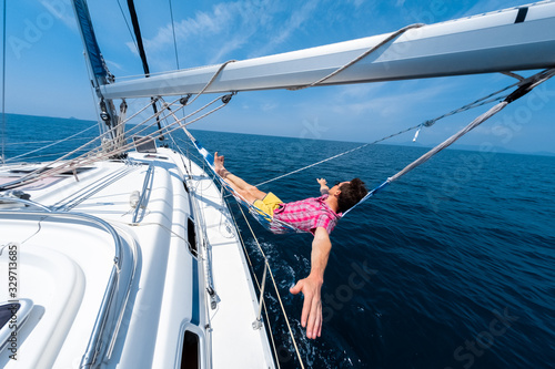 Young man enjoys tropical sailing in the hammock set on the boom of the yacht