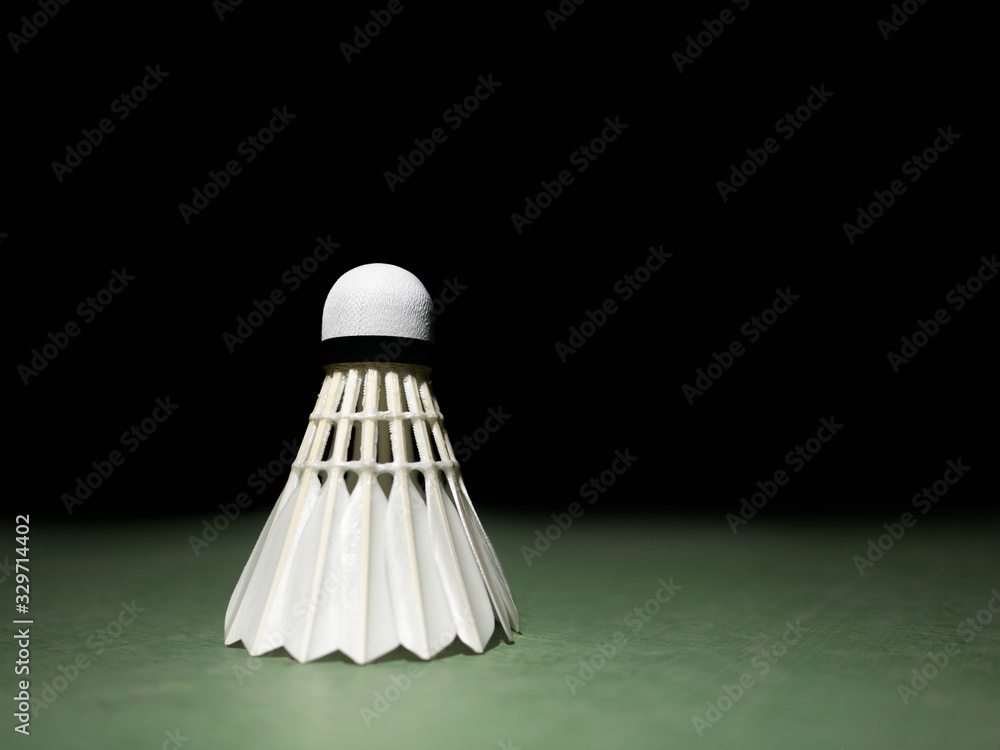 Badminton ball or shuttlecock located on the green ground with a black background. Concepts of victory or strength in training. There is space for copy space. Or enter various messages.