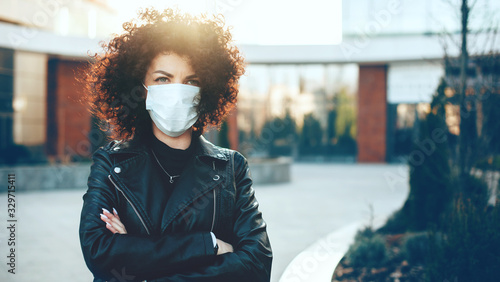 Caucasian woman posing with crossed hands while wearing an anti flu mask and looking at camera
