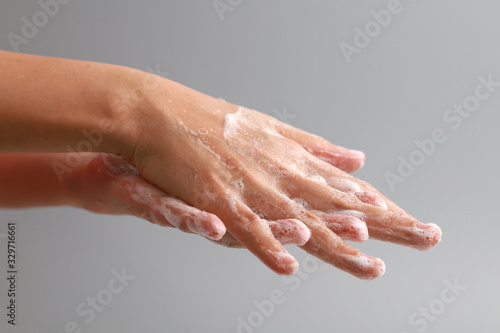 Female washing hand with soap on grey background. Good personal hygiene practices.