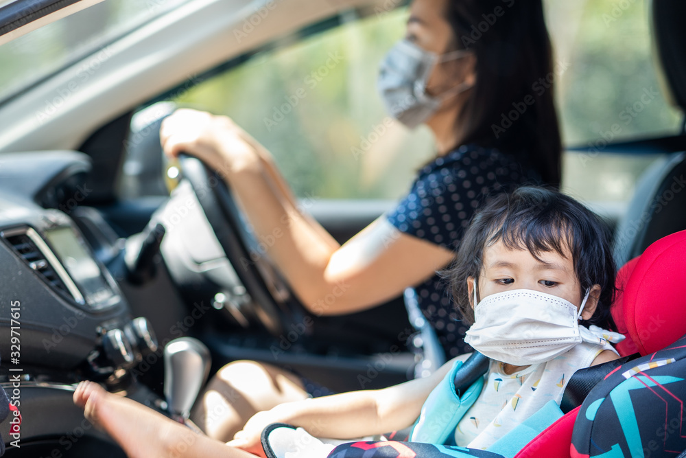 Little girl and her mother sitting in car wearing medical face mask.