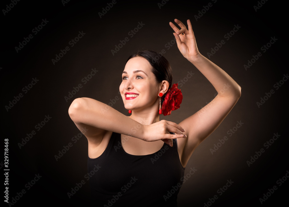 Female portrait of emotional flamenco dancer. Expressive smiling woman with hair up in a bun and red rose in black dress doing a pose. Isolated, low key.