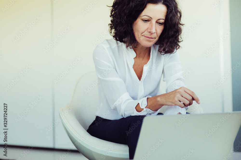 Serious focused business lady working on computer in office lounge. Business woman sitting in armchair, using laptop, looking at screen. Communication concept Serious focused business lady working on computer in office lounge. Business woman sitting in armchair, using laptop, looking at screen. Communication concept