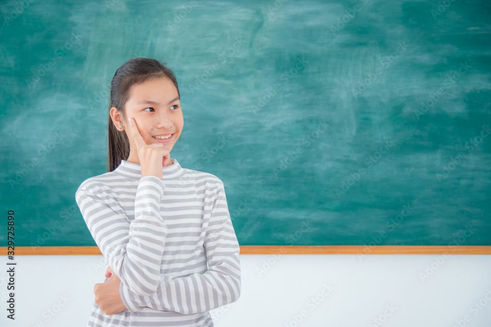 Young asian female student thinking and smiles in front of green chalkboard background. Young asian female student thinking and smiles in front of green chalkboard background.