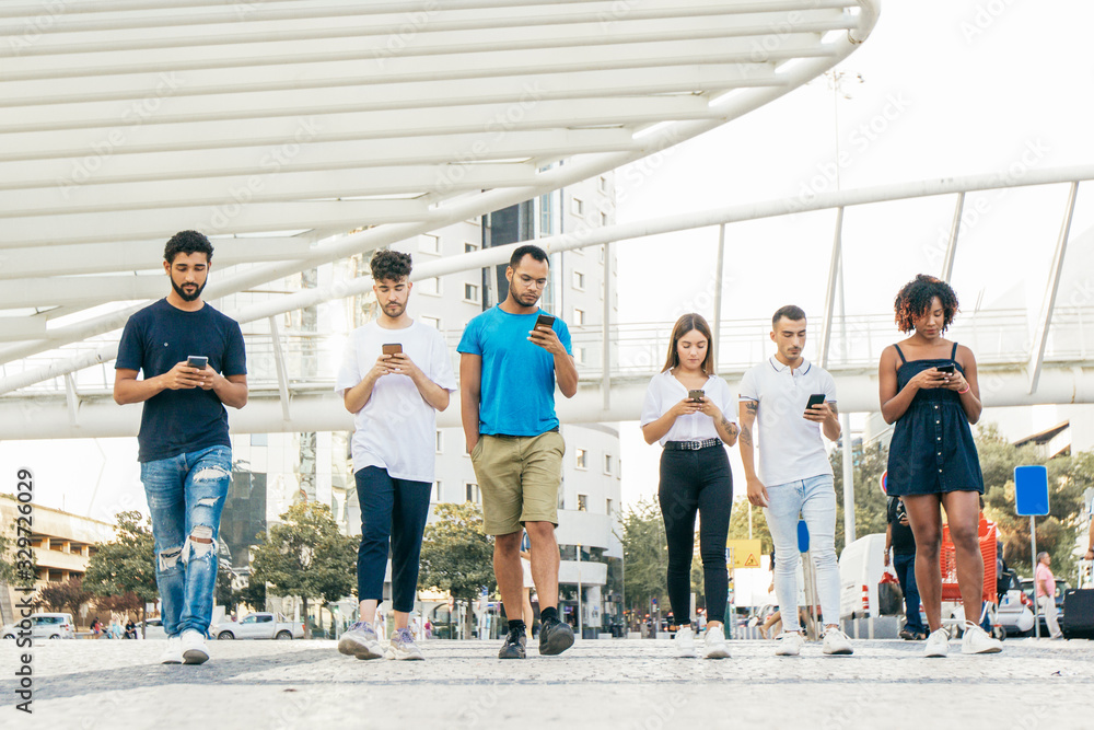 Line of people walking together and browsing internet on smartphones outside. Diverse men and women going through city square and using mobile phones. Digital communication concept