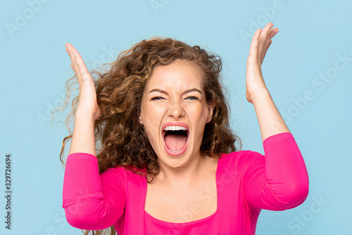 Shocked angry young Caucasian woman shouting isolated on light blue studio background