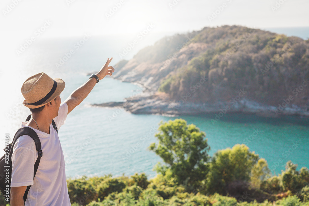 Man wearing hat holds his hand happy. Man asian tourist Look at mountains and the sea Before sunset.for activity lifestyle outdoors freedom or travel tourism inspiration backpacker tourist to covid 19