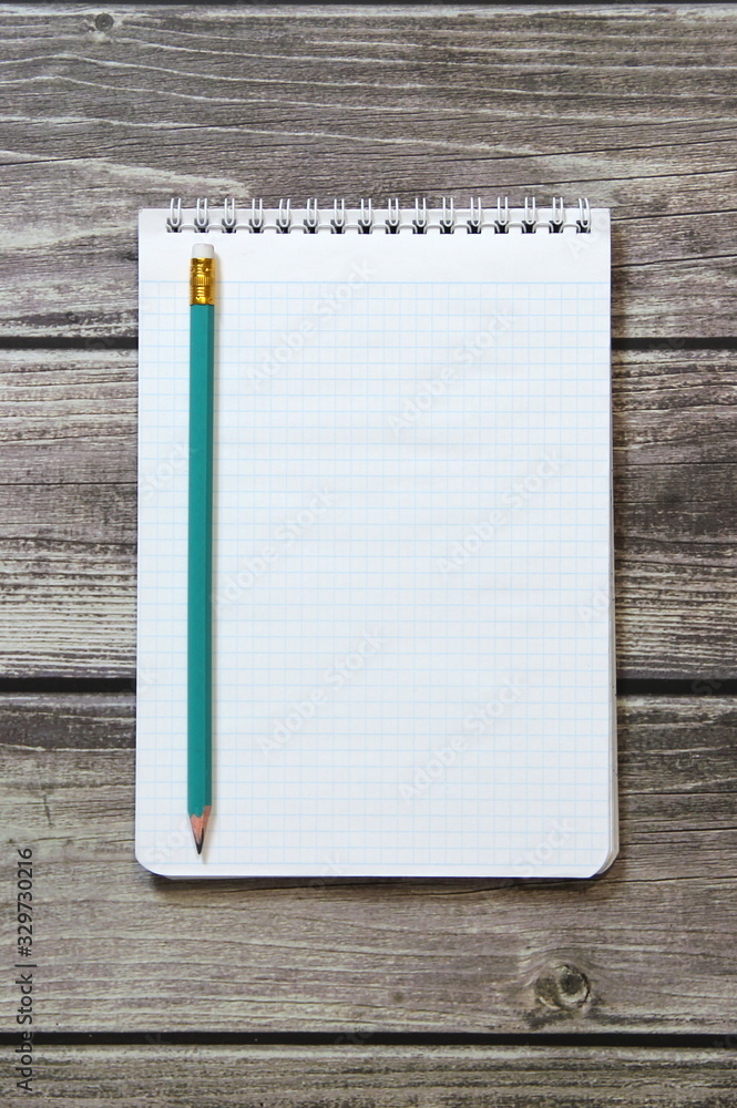 Notepad with a blank white sheet in a checker paper with simple graphite pencil lies on the background of wooden boards Notepad with a blank white sheet in a checker paper with simple graphite pencil lies on the background of wooden boards