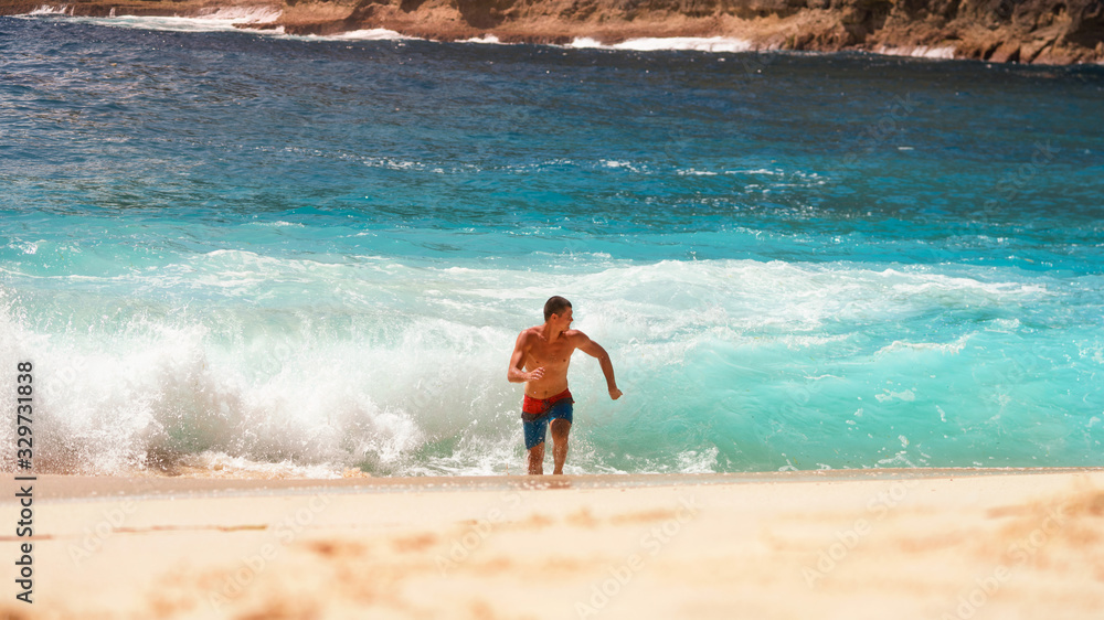 The guy is running away from the waves of the ocean in shorts on the beach sun heat The guy is running away from the waves of the ocean in shorts on the beach sun heat