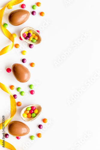 Easter background with chocolate eggs and dragees on white background top-down frame copy space