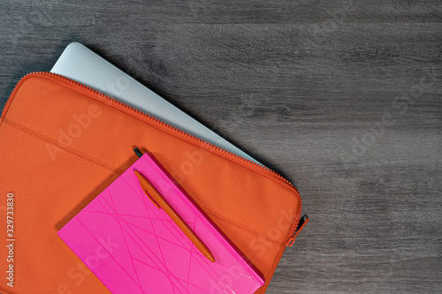 Bright orange laptop case with pink note book and pen flatlay. photo