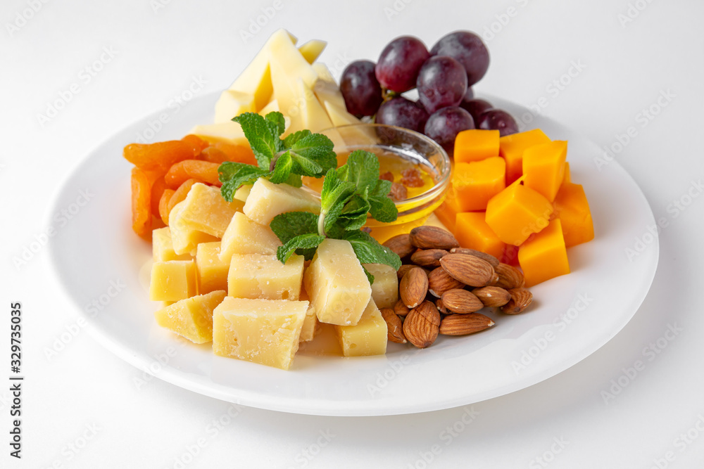 Plate with appetizer of different types of cheese, grapes and nuts with honey. Banquet festive dishes. Gourmet restaurant menu. White background.