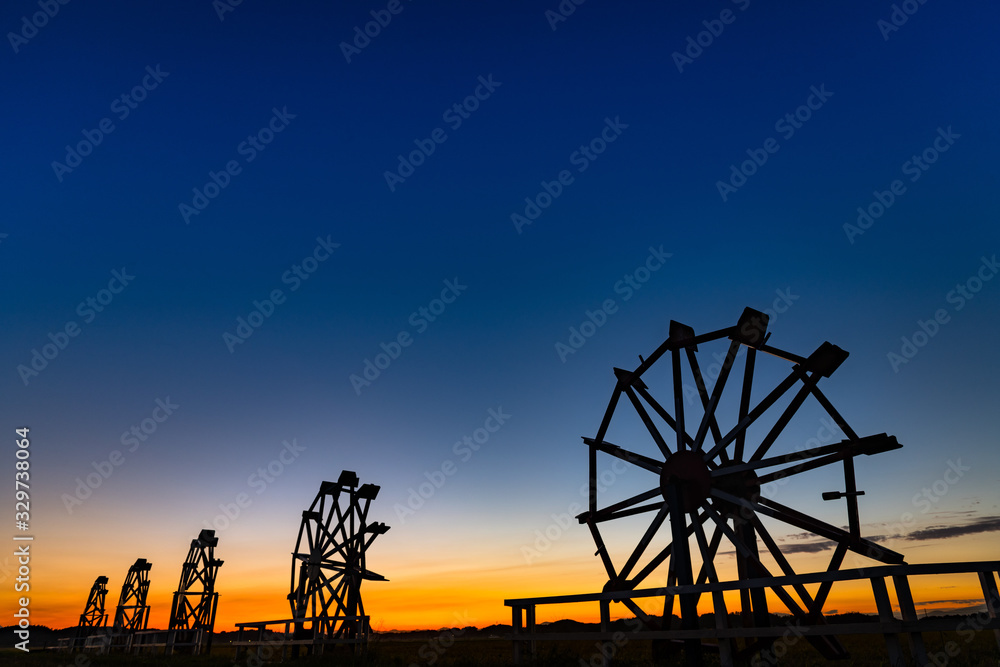 夕焼けの水田の中の水車