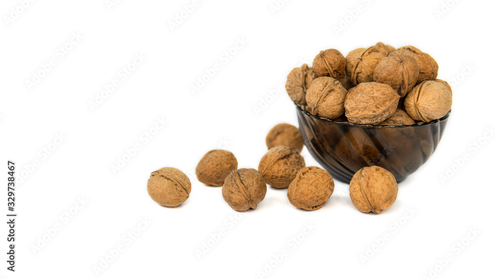Whole walnuts in dark glass bowl on white background with space for text. Side view. Beautiful walnuts near glass bowl. Whole walnuts in dark glass bowl on white background with space for text. Side view. Beautiful walnuts near glass bowl.