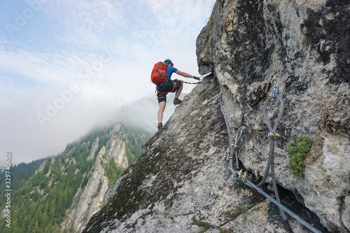 Stunning shot of a young man climbing up a cliff on a cold and foggy day photo