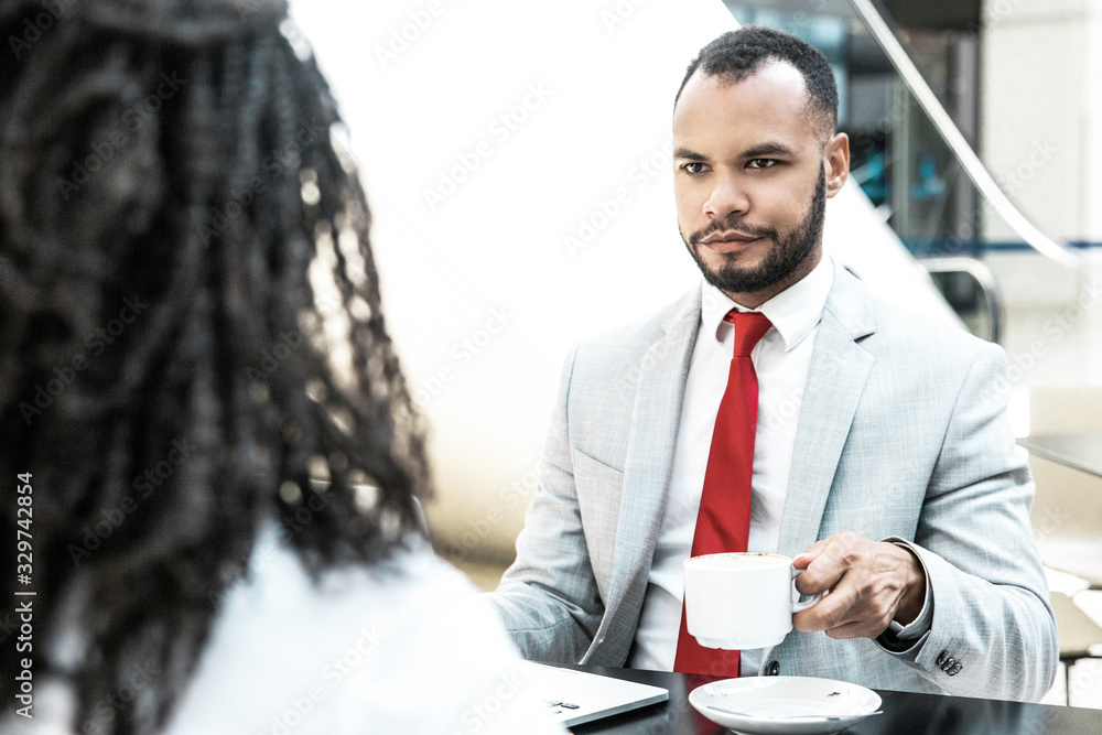 Businessman discussing deal with partner over cup of coffee. Business man sitting at table opposite of his female colleague and drinking coffee. Corporate coffee break concept Businessman discussing deal with partner over cup of coffee. Business man sitting at table opposite of his female colleague and drinking coffee. Corporate coffee break concept