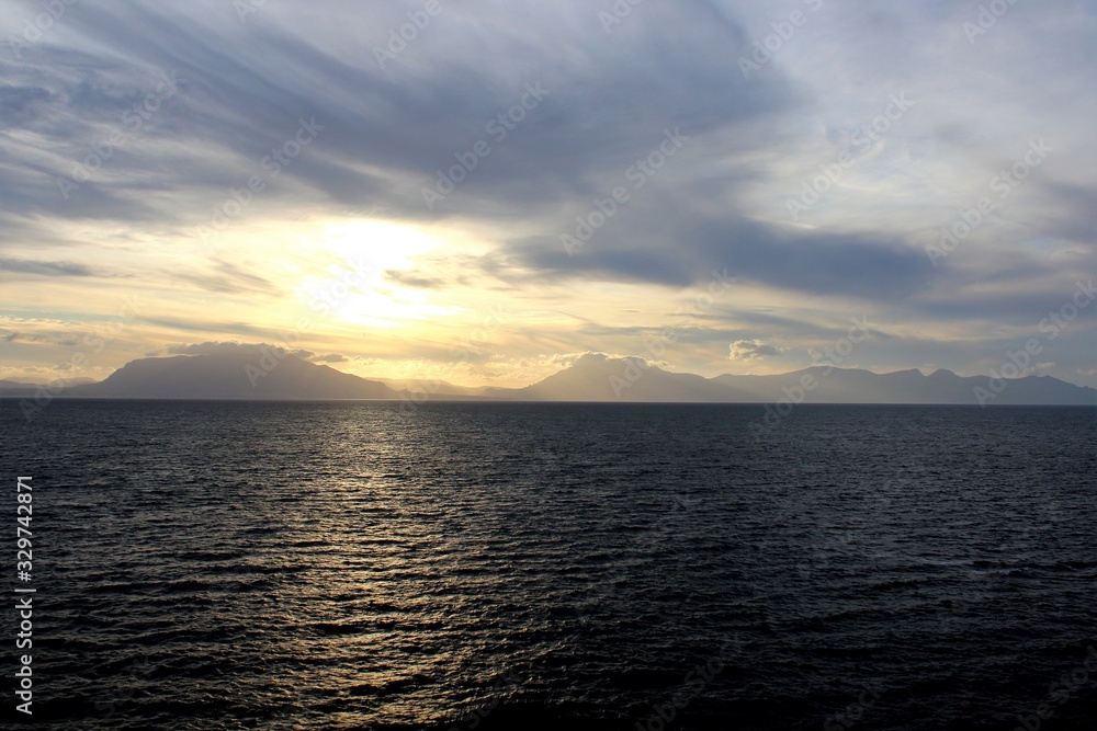 evocative image of sunset over the sea with headland silhouette in the background evocative image of sunset over the sea with headland silhouette in the background