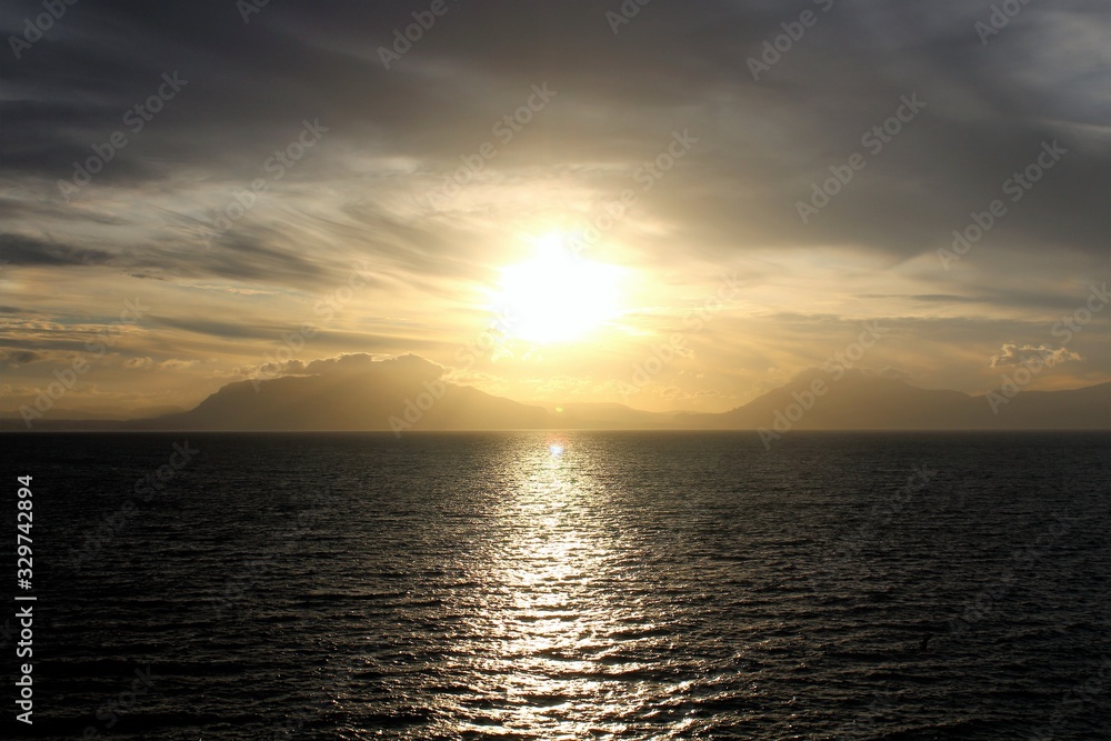 Naklejka premium evocative image of sunset over the sea with headland silhouette in the background