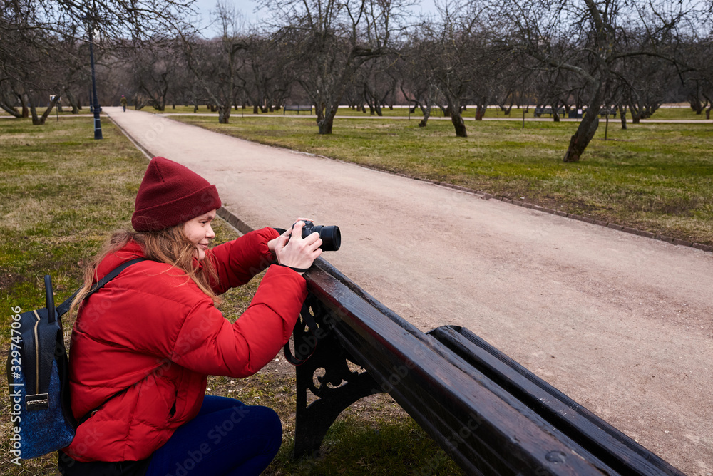  girl in a red jacket takes pictures on camera in the park in spring