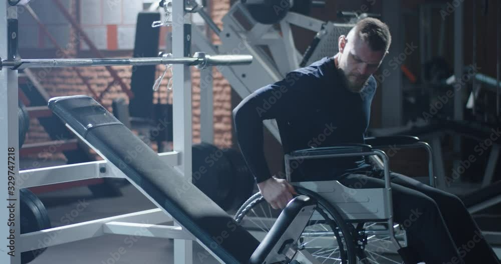 Disabled man moving from wheelchair to training bench Disabled man moving from wheelchair to training bench