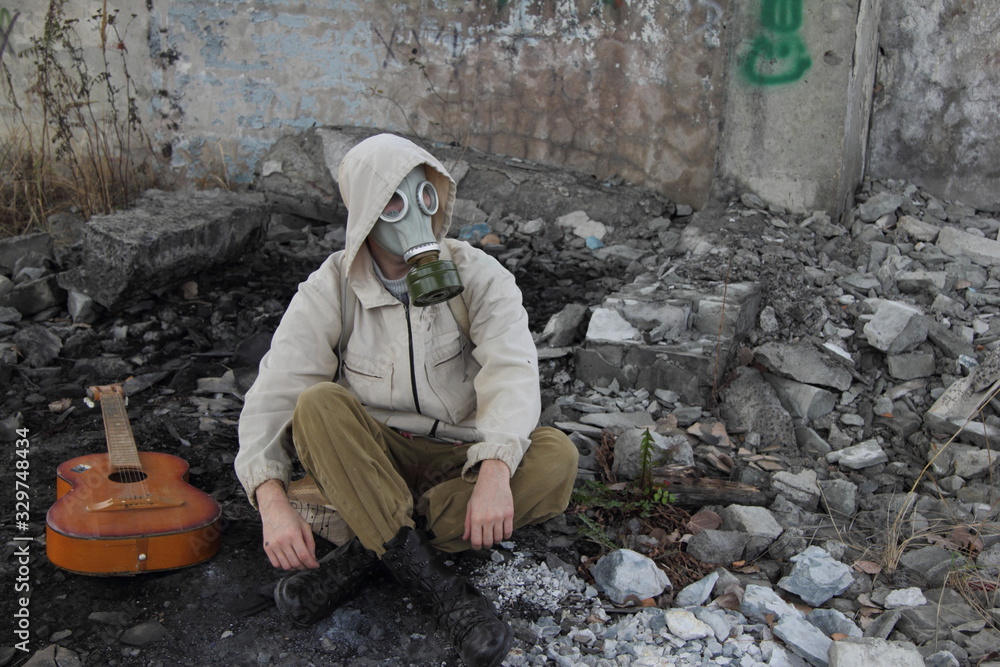The artistic concept of post-apocalypse - a man in a gas mask sits among concrete ruins with a guitar. The artistic concept of post-apocalypse - a man in a gas mask sits among concrete ruins with a guitar.
