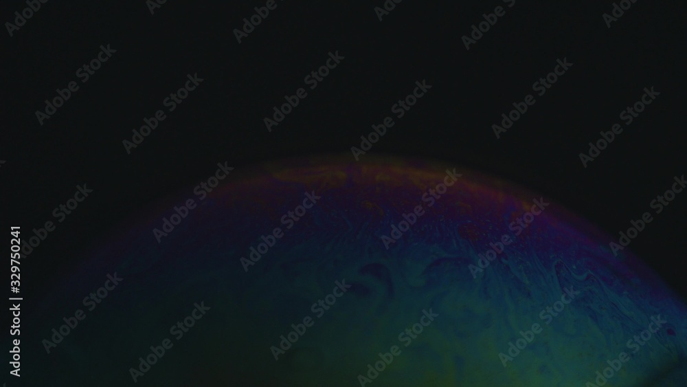 Rainbow soap bubble on a dark background. Close-up of colorful surface