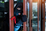 masked burglar with crowbar breaking and entering into a victim's home