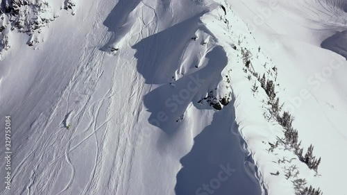 A man skiing down the beautiful snow white mountain slope near Whistler, Canada on a bright winter day - Aerial shot photo