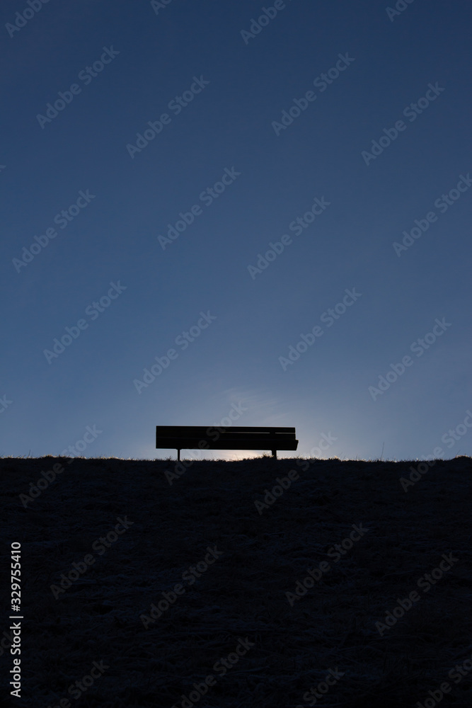 Silhouette of a empty bench on a hill in front of a clear dark blue sky