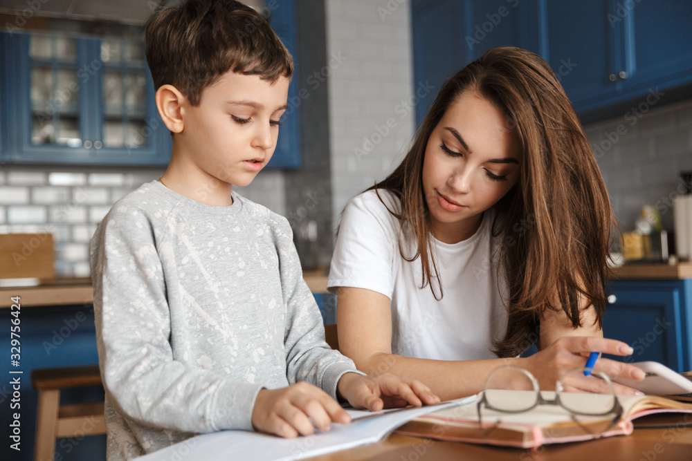 Image of nice woman and cute boy reading exercise while doing homework Image of nice woman and cute boy reading exercise while doing homework