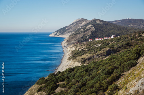 Mountainous rocky seashore covered with juniper forest in summer. A steep cape with an adjacent quiet bay and a stone beach.